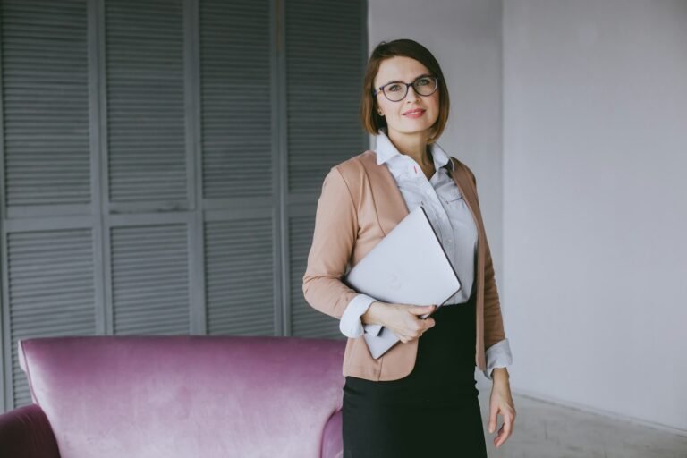 Woman in smart business attire holding a laptop at work